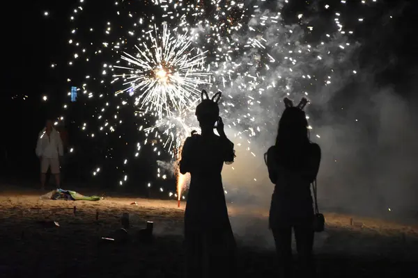 stock image Houhai, Hainan, China - April 4 2021: Two women with their backs to the camera stand in front of a fireworks display on the beach in Houhai on Hainan Island.