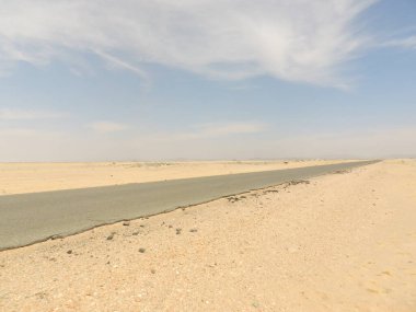 Moritanya 'da mavi bir gökyüzünün altında Sahra Çölü' nün kumu boyunca bir yol kesiliyor..