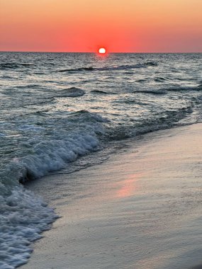 Denizde gün batımı, sahilde dalgalar, turuncu gökyüzü.