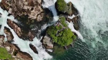 Denizin ortasında yeşilliklerle çevrili bir şelalenin dikey görüntüsü.