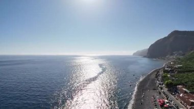 Arka planda deniz ve kayalıkları olan bir plajın havadan çekilmiş görüntüleri Cascata dos Anjos ve plajın üzerinde uçuyor. Portekiz 'in Madeira adasının güneyinde iki gizli şelale..