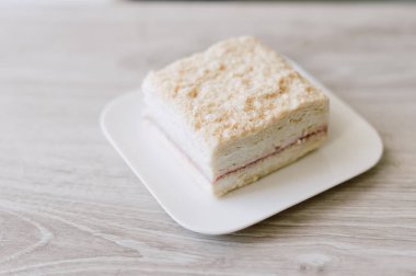 Beyaz bir tabakta bir parça kek duruyor. Pasta kare şeklinde kesilmiş.