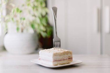 Bir çatal, beyaz bir tabakta bir parça kekin içinden sarkıyor. Çatal üstte bükülmüş ve pasta kare şeklinde kesilmiş.