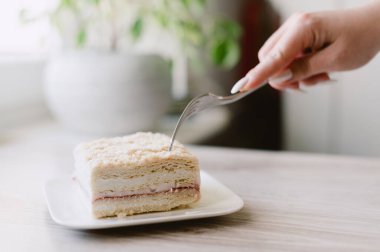 Birisi çatalla bir parça pasta kesiyor. Pasta beyaz tabakta.