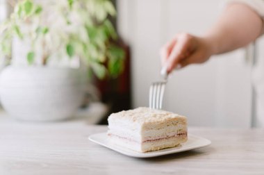 Birisi çatalla bir parça pasta kesiyor. Pasta beyaz tabakta.