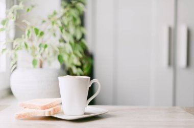 Üzerinde beyaz bir tabak olan beyaz bir kahve fincanı. Tabakta iki parça tost var.
