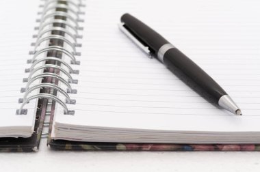 Siyah bir kalem, spiral kaplı bir defterin beyaz sayfasında. Kalem sayfada duruyor ve kullanımda değil