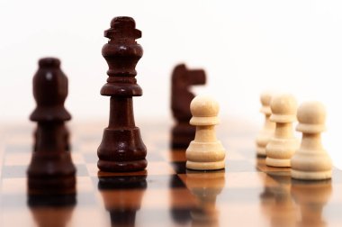 Siyah ve beyaz bir satranç taşı siyah ve kahverengi bir taşla tahta bir tahtanın üzerinde duruyor. Siyah ve beyaz parça bir piyon, tahtanın en küçük ve en az güçlü parçası.