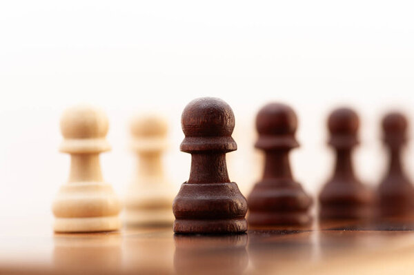Черно-белая шахматная фигура стоит на доске с другими фигурами. Это пешка, самая маленькая и наименее мощная фигура на доске. Пешка располагается посередине доски