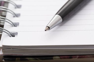 Spiral kaplı bir defterin üzerinde bir kalem duruyor. Kalem siyah ve gümüş uçlu.