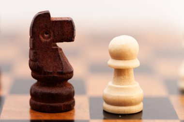 Siyah başlı ahşap bir satranç taşı ve kareli tahtaya beyaz bir beden yerleştiriliyor.