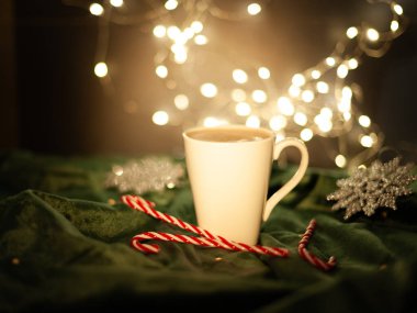 Yanında kırmızı ve beyaz çizgili bir değnek olan beyaz bir kahve fincanı. Sahne bir Noel ortamında geçiyor.