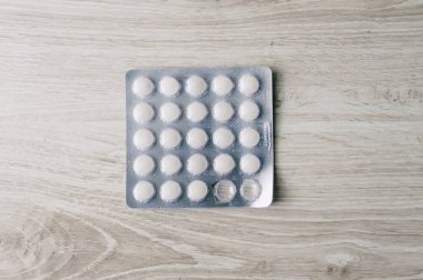 Tahta bir masanın üzerinde bir kutu hap var. Haplar beyaz ve kare şeklinde.