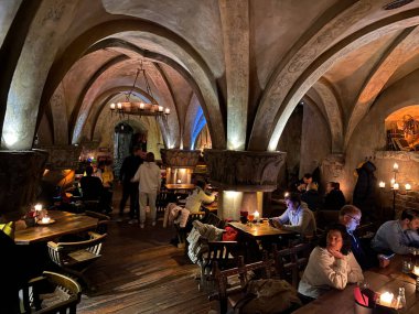 Masalarda bir sürü insanın oturduğu bir restoran. Masaların üzerinde bir sürü mum var. Bir kadın cep telefonuyla bir masada oturuyor. Letonya, Riga 08.10.2023