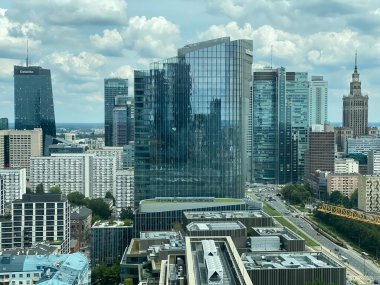 Ortada yüksek bir bina olan Varşova silueti. Gökyüzü bulutlu ve şehir hareketlilik içinde.