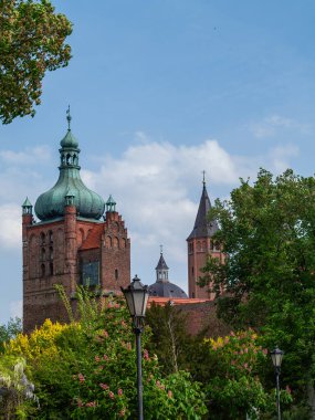 Yeşil kubbeli büyük bir tuğla bina yemyeşil bir parkın önünde duruyor. Bina ağaçlar ve bir lamba direği ile çevrilidir. Sahne huzurlu ve huzurlu, insanlar banklarda oturuyor.