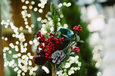 Kırmızı ve yeşil bir Noel süslemesi, kozalaklı ve elmalı. Elma dekorasyonun sol tarafında ve çam kozalağı da sağ tarafında.