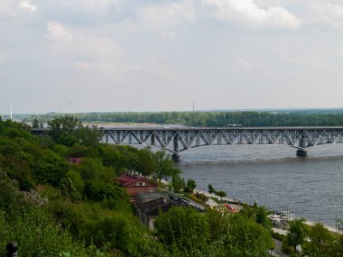 Köprü, arka planda bir kasaba olan bir nehri kapsar. Köprü, üzerinde birkaç araba bulunan büyük bir çelik yapıdır.
