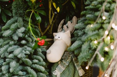 Beyaz bir geyik kırmızı böğürtlenlerle bir çalılıkta duruyor. Geyik yeşil bir eşarp takıyor.