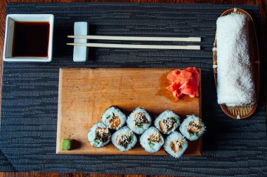 Çubuklu bir tabak suşi ve küçük bir kase sos. Suşi ahşap bir tahtada ve tahtada birkaç parça suşi var.