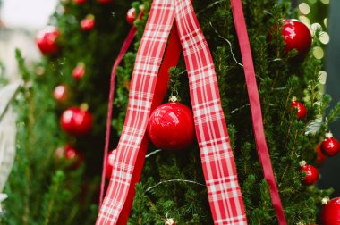 Kırmızı ve beyaz bir ekose kurdele bir Noel ağacının etrafına sarılmış. Kurdeleden sarkan birkaç kırmızı ve beyaz top var.