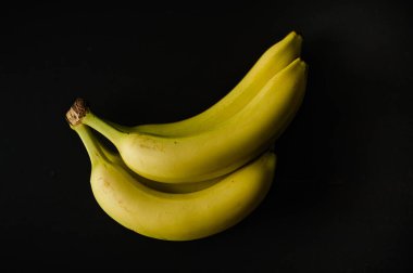 Siyah bir arka planda oturan üç muz. Muzlar sarı ve olgun görünüyor. Ana odak noktası muzlar olduğu için görüntüde basit ve doğal bir his var.