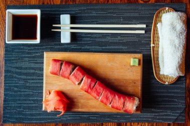 Çubuklu bir tabak suşi ve masanın üstünde peçete. Suşi uzun şeritlere ayrılır ve yanında sosu da eklenir.