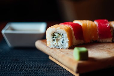 Üzerinde yeşil yosun olan bir suşi rulosu. Suşi rulosu yanında beyaz bir kâseyle ahşap bir kesme tahtasının üzerinde.