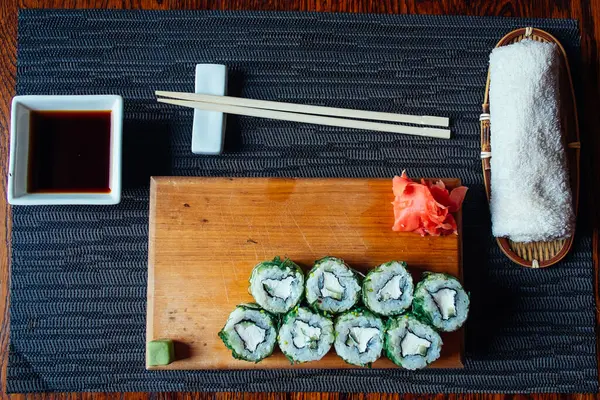 Çubuklu bir tepsi suşi ve sos. Suşi ahşap bir tahta üzerine kurulmuş ve etrafı siyah bir bezle çevrili.