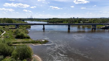 Köprü, arka planda bir şehir bulunan bir nehri kapsar. Köprü nehrin iki tarafını birbirine bağlayan büyük bir yapıdır. Varşova 20.04.2025 Polonya ülkesi