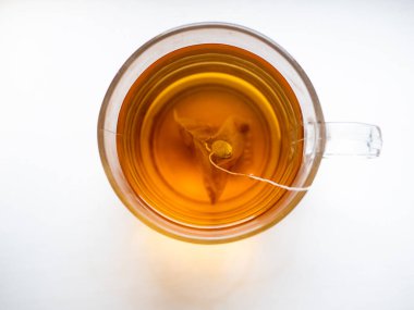 İçinde çay poşeti olan bir fincan çay. Bardak berrak bardaktan yapılmıştır ve çay sıcak, altın renktedir.