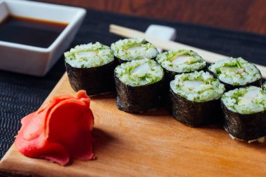 Üzerinde kırmızı çiçek olan bir tabak suşi. Suşi ahşap bir tahtanın üzerinde ve yanında bir kase sos var.