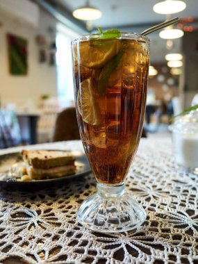 Bir bardak kireç dilimli çay masanın üzerinde duruyor. Masa dantel altlık ve bir tabak yemekle kaplı.