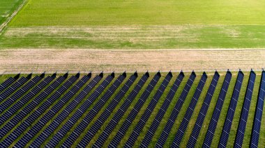 Görüntüde güneş panellerinin alanı gösteriliyor. Paneller sıra sıra dizilir ve çimlerle çevrilidir. Sürdürülebilirlik ve çevresel bilinç kavramı. Havadan