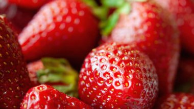 Bir sürü kırmızı çilek yakın çekim. Çilekler taze ve olgun, parlak kırmızı bir renkle. Bereket ve tazelik kavramı, çilekler üst üste yığılmış ve yenmeye hazır.