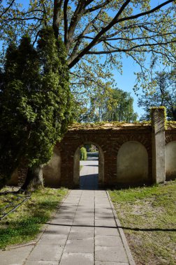 Küçük kemerli tuğla duvar ve önünde bir ağaç. Kemer yolu açık.