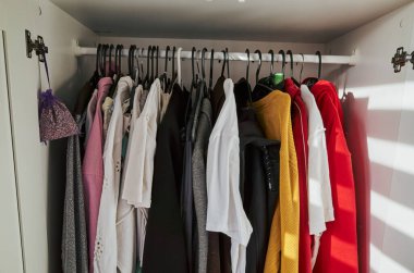 Dolabın sol tarafında beyaz bir gömlek ve sağ tarafında da kırmızı bir gömlek asılı.