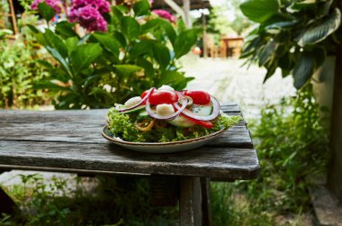 Bir tabak salata, domates, salatalık ve soğan dışarıda ahşap bir masada duruyor.