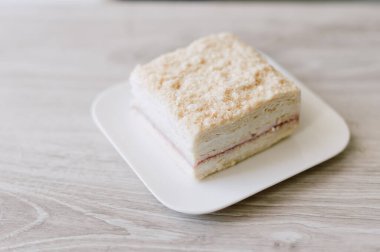 Beyaz bir tabakta bir parça kek duruyor. Pasta kare şeklinde kesilmiş.