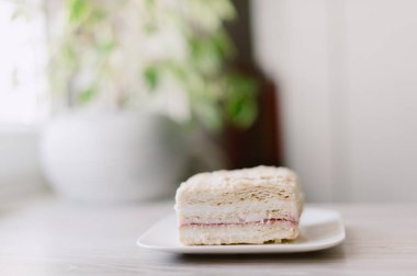 Bir dilim kek beyaz bir tabakta. Pasta ikiye bölünmüş ve arkasında yeşil bir bitki var.