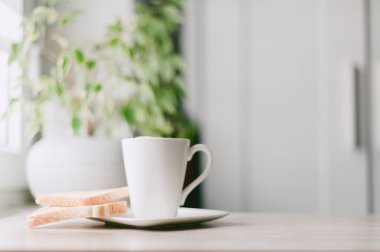 Üzerinde beyaz bir tabak olan beyaz bir kahve fincanı. Tabakta iki parça tost var.