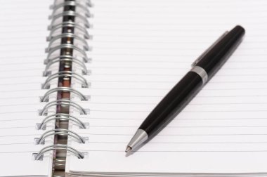 Siyah bir kalem, spiral kaplı bir defterin beyaz sayfasında. Kalem sayfada duruyor ve kullanımda değil