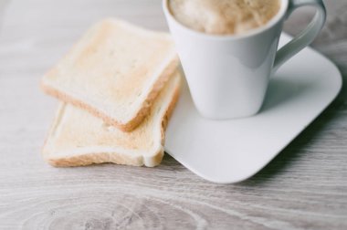 Üzerinde beyaz bir tabak olan beyaz bir kahve fincanı. Tabakta iki parça tost var.