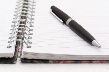 Siyah bir kalem, spiral kaplı bir defterin beyaz sayfasında. Kalem sayfada duruyor ve kullanımda değil