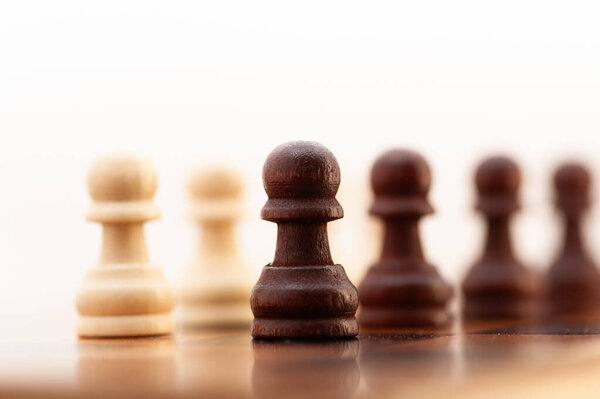 Черно-белая шахматная фигура стоит на доске с другими фигурами. Это пешка, самая маленькая и наименее мощная фигура на доске. Пешка располагается посередине доски