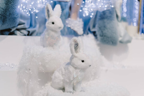 Два белых кролика сидят на куче снега. Один из кроликов смотрит в камеру.