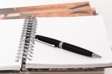 Siyah bir kalem, spiral kaplı bir defterin beyaz sayfasında. Kalem sayfada duruyor ve kullanımda değil