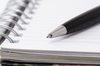 Spiral kaplı bir defterin üzerinde bir kalem duruyor. Kalem siyah ve gümüş uçlu.