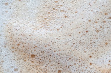 Kahverengi köpük kıvrımlı beyaz bir arka plan. Köpük baloncuklardan oluşur. Kabarcıklar küçük ve köpüğe saçılmış.