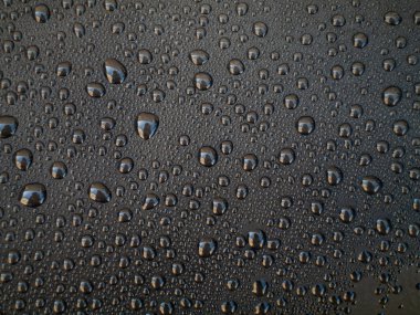 Bir sürü küçük su damlası olan siyah bir yüzeye yakın çekim. Damlalar tüm yüzeye saçılmış.